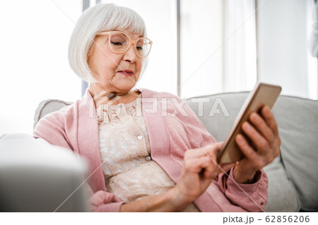 Senior lady using modern cellphone at home 62856206