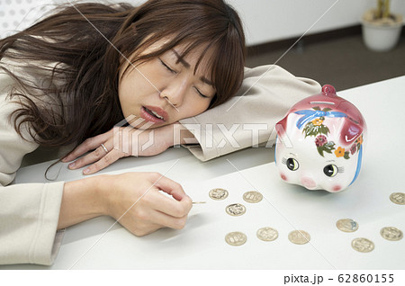 お金のことで悩む若い女性と貯金箱 お金のことで悩む若い女性と貯金箱 62860155