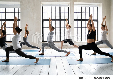Multi-ethnic group of young people performing Warrior 1 yoga position 62864369