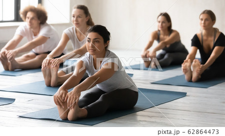 Group of people sitting in mats performing Seated Forward Bend 62864473