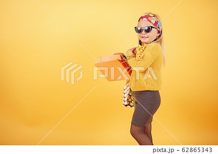 Cute little girl with shopping bags on a yellow background Cute little girl with shopping bags on a yellow background 62865343
