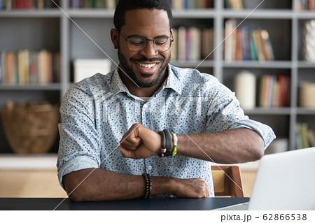 Smiling millennial african american man checking time on wristwatch. 62866538