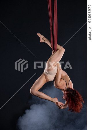Female athletic, sexy and flexible aerial circus artist with redhead dancing in the air on the silk 62868979