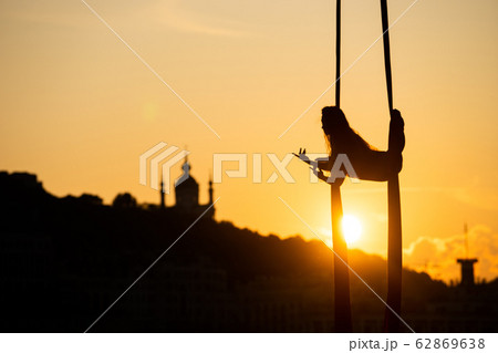 Silhouette of a flexible woman acrobat on aerial silk during a sunset on Kiev city background 62869638