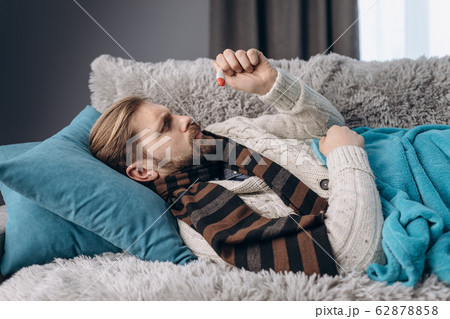 Mature man lying on couch and looking at thermometer 62878858