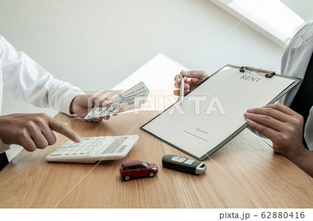 Car dealership provides advice about insurance details and car rental information and delivers the keys after signing the rental contract 62880416