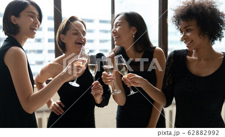 Happy diverse women wearing elegant black dresses clinking champagne glasses Happy diverse women wearing elegant black dresses clinking champagne glasses 62882992