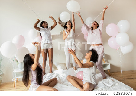 Happy diverse girls playing with balloons in bedroom at party Happy diverse girls playing with balloons in bedroom at party 62883075