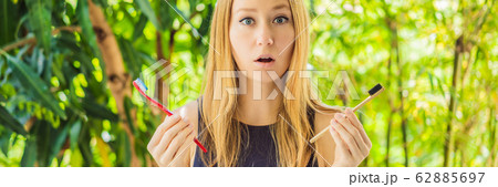BANNER, LONG FORMAT Woman holds eco natural bamboo toothbrush and in other hand plastic toothbrush BANNER, LONG FORMAT Woman holds eco natural bamboo toothbrush and in other hand plastic toothbrush 62885697