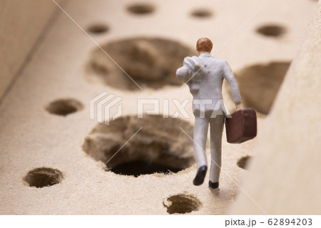 沢山の落とし穴を避けながら走るビジネスマン 62894203