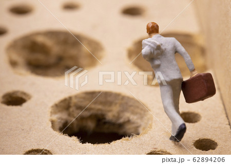 沢山の落とし穴を避けながら走るビジネスマン 62894206