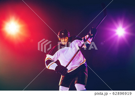 Male hockey player with the stick on ice court and dark neon colored background Male hockey player with the stick on ice court and dark neon colored background 62896919