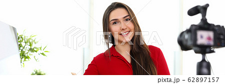 Young woman sitting in office opposite camera on tripod Young woman sitting in office opposite camera on tripod 62897157