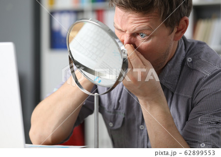 Man sits in front mirror and presses on his face Man sits in front mirror and presses on his face 62899553