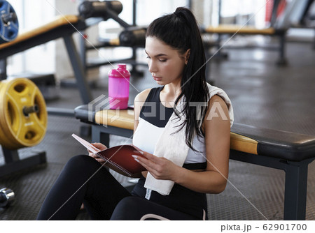 Workout planning. Young woman with notebook resting after training in gym Workout planning. Young woman with notebook resting after training in gym 62901700