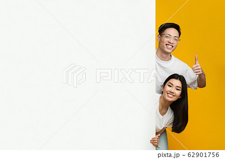 Asian happy couple standing next to empty advertising board 62901756