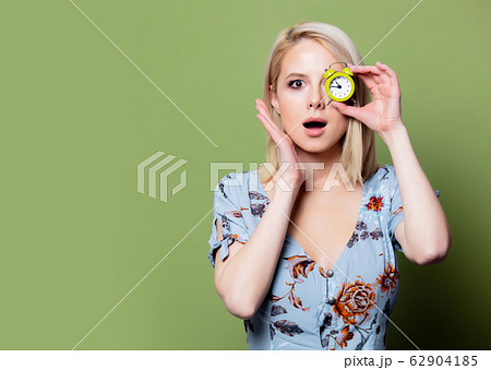 Blonde woman with alarm clock on green background Blonde woman with alarm clock on green background 62904185