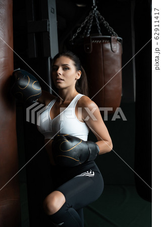 Boxing woman posing with punching bag, on dark background. Strong and independent woman concept Boxing woman posing with punching bag, on dark background. Strong and independent woman concept 62911417