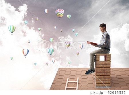 Handsome student guy reading book and aerostats flying in air Handsome student guy reading book and aerostats flying in air 62913532