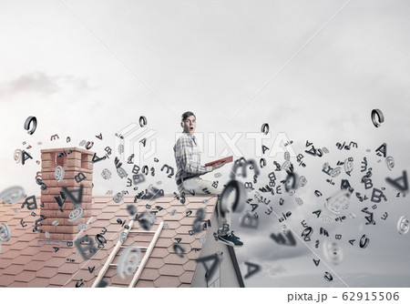 Man on brick roof reading book and symbols flying around Man on brick roof reading book and symbols flying around 62915506