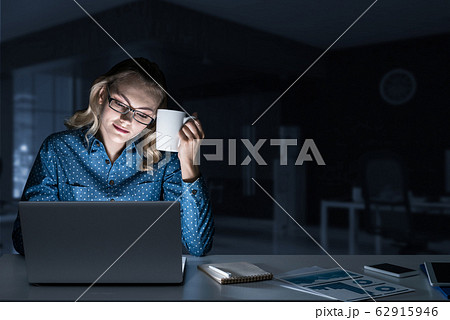 Attractive blonde working on laptop in dark office. Mixed media Attractive blonde working on laptop in dark office. Mixed media 62915946