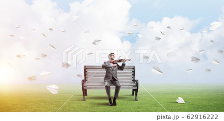 Handsome violinist in park on wooden bench play his melody Handsome violinist in park on wooden bench play his melody 62916222