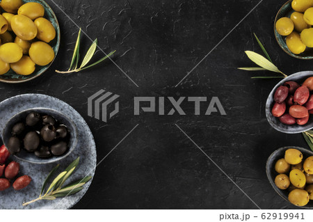 Olives, green, black and red, an assortment with leaves on a dark table with a place for text, a flat lay design template Olives, green, black and red, an assortment with leaves on a dark table with a place for text, a flat lay design template 62919941
