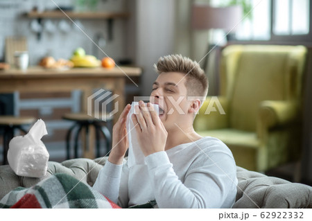 Fair-haired young man holding a napkin and sneezing Fair-haired young man holding a napkin and sneezing 62922332