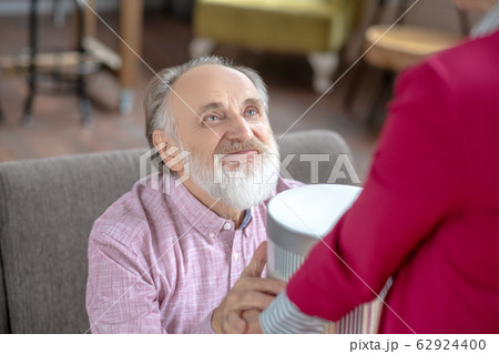 Grey-haired bearded man looking happy taking a gift from his wife 62924400