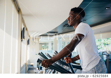Side view of fit African American man in sportswear doing steps on elliptical machine during workout in modern gym Side view of fit African American man in sportswear doing steps on elliptical machine during workout in modern gym 62925684