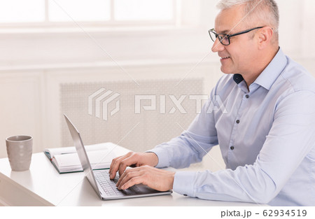 Happy senior man using laptop at home office 62934519