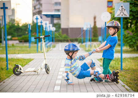 two boys in park, help boy with roller skates to 62936734