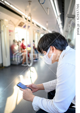 Asian man wearing mask using phone on skytrain Asian man wearing mask using phone on skytrain 62937766