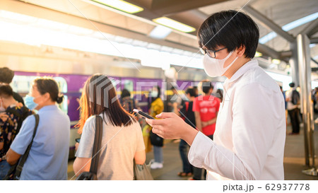 Man wearing mask using phone at skytrain station Man wearing mask using phone at skytrain station 62937778