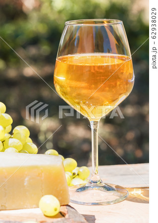 Beautiful still life with amber wine in glasses on the nature: a bright summer drink with cheese and grapes in a rustic style. 62938029