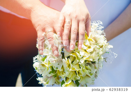 Close-up Bride and groom's hands with wedding rings and bouquet. Love and marriage. Wedding accessories and decor on the background of the river 62938319