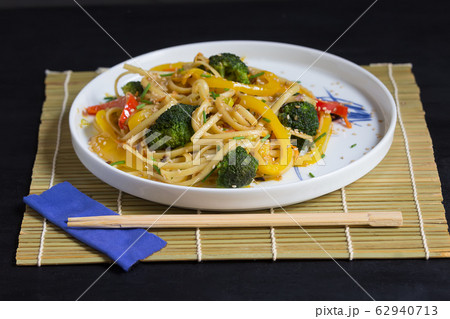 Stir fry noodles with vegetables and soy sauce on bamboo mat, black background 62940713