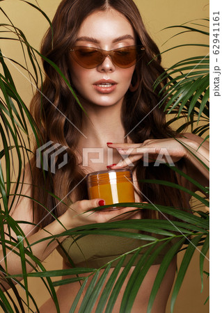Beautiful sexy woman in a bikini posing in the middle of green plants with a box of cosmetics in hand. Summer look. Beauty face Beautiful sexy woman in a bikini posing in the middle of green plants with a box of cosmetics in hand. Summer look. Beauty face 62941161