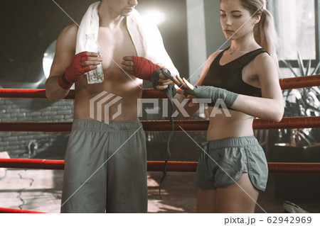 Portrait of a couple of boxers taking a break and resting in a boxing gym. Man holding a bottle of water and towel talking with his partner woman wearing boxinf bandages 62942969