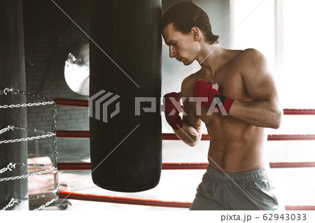 Male boxer boxing in punching bag. The boxer touches his head to the punching bag. 62943033