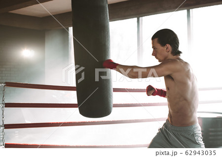 angry boxer standing in boxing pose near punching bag on black with smoke angry boxer standing in boxing pose near punching bag on black with smoke 62943035