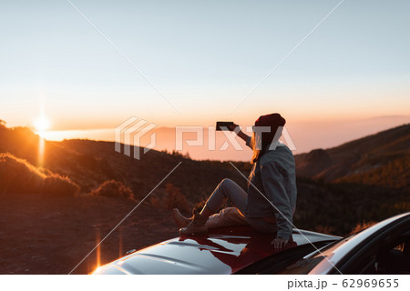 Woman enjoying beautiful sunset while traveling in the mountains by car Woman enjoying beautiful sunset while traveling in the mountains by car 62969655
