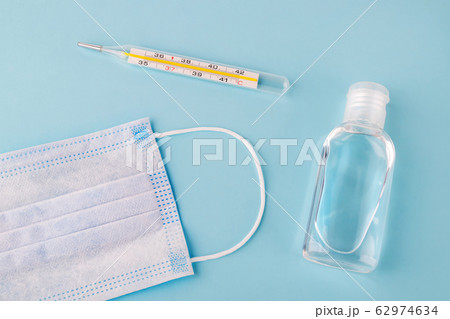 Disposable surgical mask, thermometer and antibacterial hand gel on a blue background. 62974634