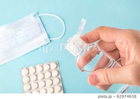Woman hand holds antibacterial hand gel over a blue surface with surgical mask and pills. 62974638