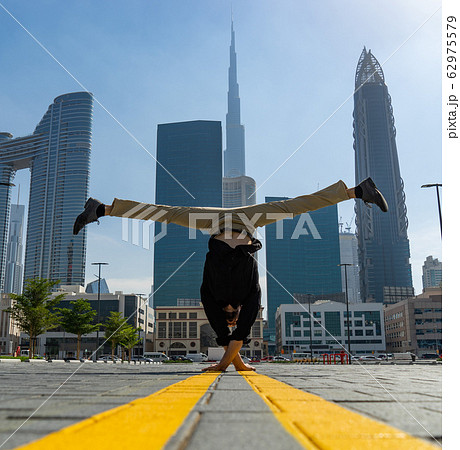 Acrobat keep balance one the hands with blurred Dubai cityscape. Concept of modern, business and Acrobat keep balance one the hands with blurred Dubai cityscape. Concept of modern, business and 62975579