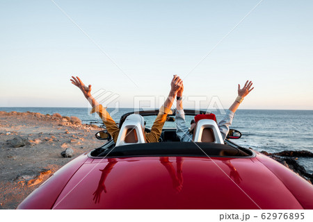 Couple driving convertible car near the ocean Couple driving convertible car near the ocean 62976895