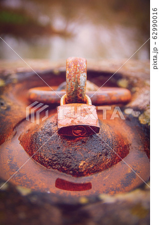 Rusty padlock locked around an aged iron ring 62990016