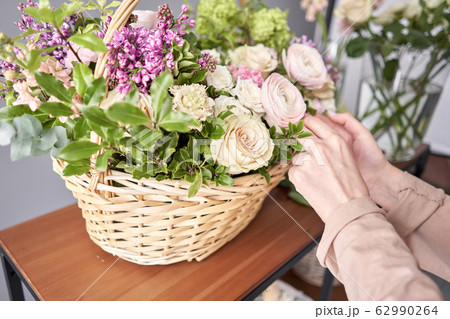 Floral shop concept . Florist woman creates flower arrangement in a wicker basket. Beautiful bouquet of mixed flowers. Handsome fresh bunch. Flowers delivery. Floral shop concept . Florist woman creates flower arrangement in a wicker basket. Beautiful bouquet of mixed flowers. Handsome fresh bunch. Flowers delivery. 62990264