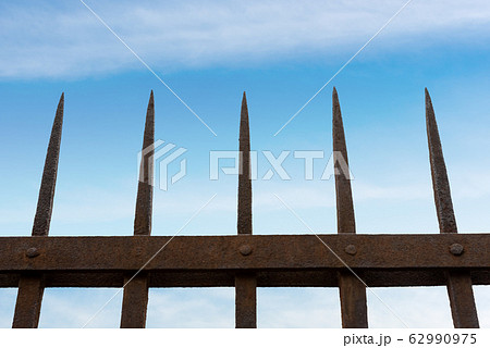 Wrought iron fence with sharp points on blue sky with clouds 62990975