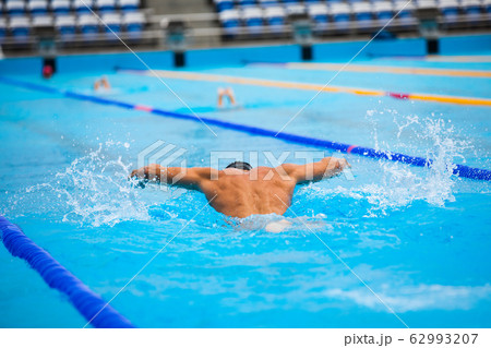 Athletic man swimming in butterfly style in the swimming pool with clear blue water. Athletic man swimming in butterfly style in the swimming pool with clear blue water. 62993207